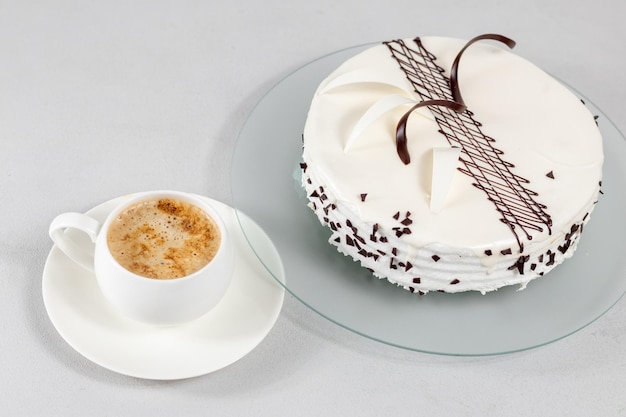 A cup of coffee and a white cake decorated with chocolate decor on a glass plate on a gray background Selective focus