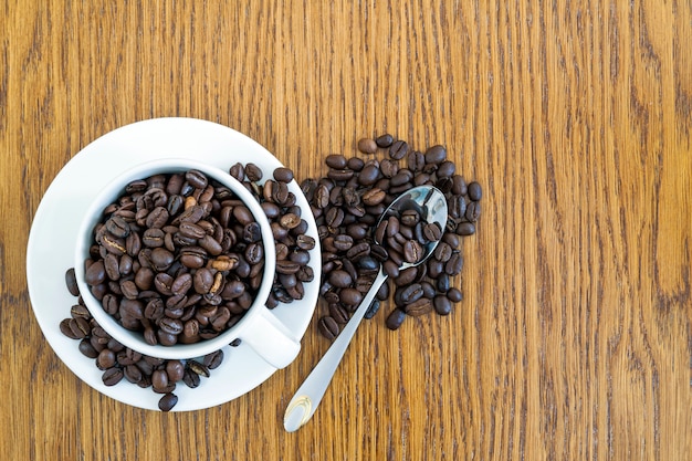 Cup of coffee in a white cup and coffee beans on wooden table background, top view.