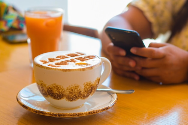 Cup of coffee with a background of some hands using a cell phone