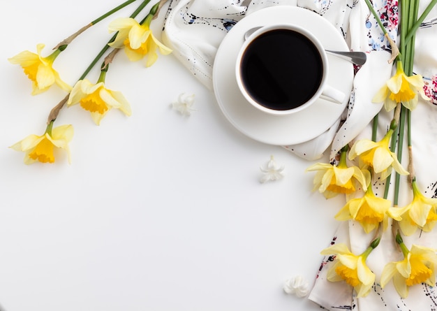 cup of coffee with beautiful narcissus flowers on the white table