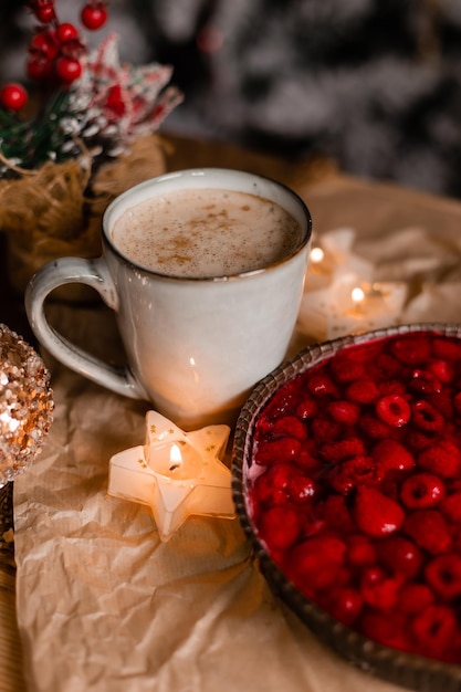 A cup of coffee with a bowl of red berries next to it