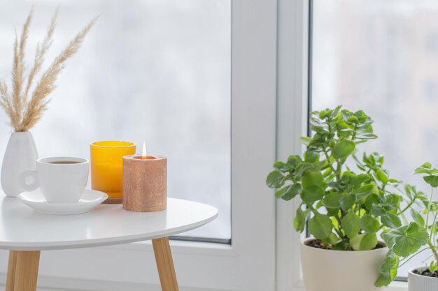 cup of coffee with burning candles on white table by window on winter