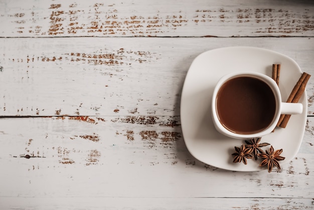 Cup of coffee with cinnamon sticks on a light wooden background