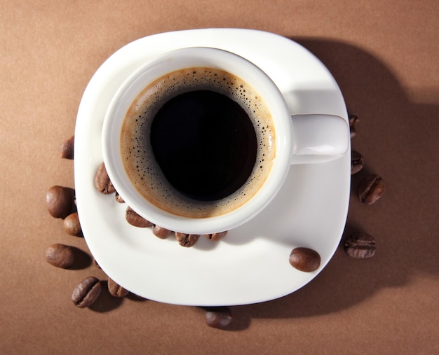 Cup of coffee with coffee beans on brown background