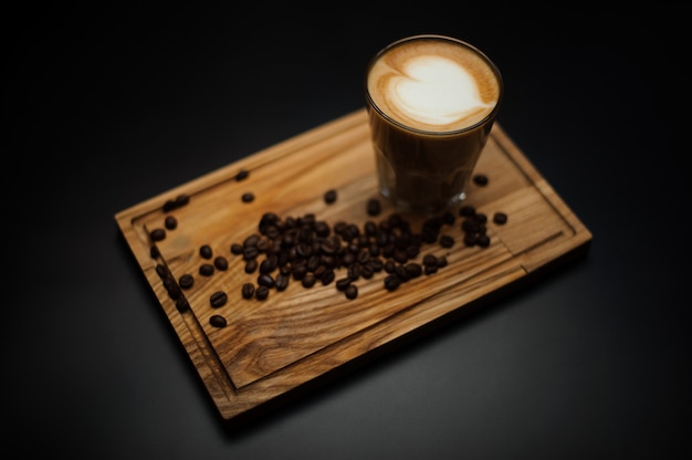 A cup of coffee with coffee beans and cane sugar on a wooden board.