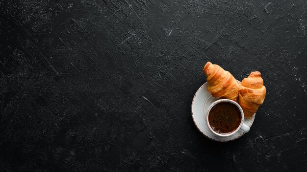 Cup of coffee with croissant Breakfast On a black stone background Top view Free space for your text