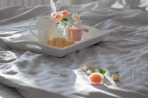 Cup of coffee with croissant  and pink roses on bed in  bedroom