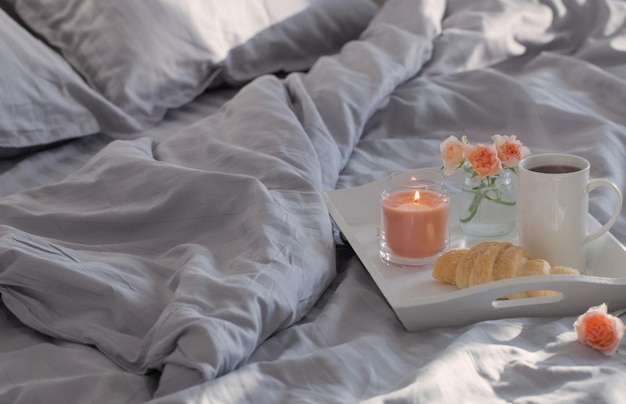 cup of coffee with croissant  and pink roses on bed in  bedroom