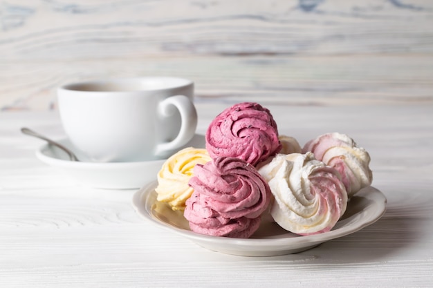 A cup of coffee with and delicious homemade marshmallows of different flavors on wooden table.