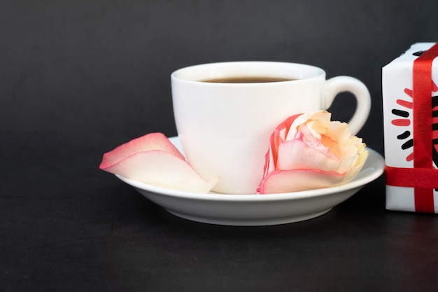 Cup of coffee with gifts, sweets and rose petals.