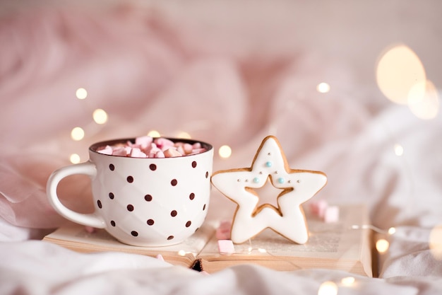 Cup of coffee with ginger bread in star shape on open book over glowing lights closeup. Winter holiday season. Xmas. Good morning.