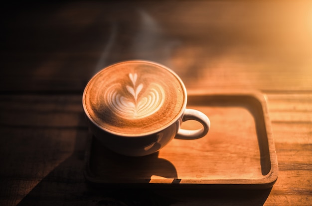 A cup of coffee with heart pattern in a white cup on wooden table background