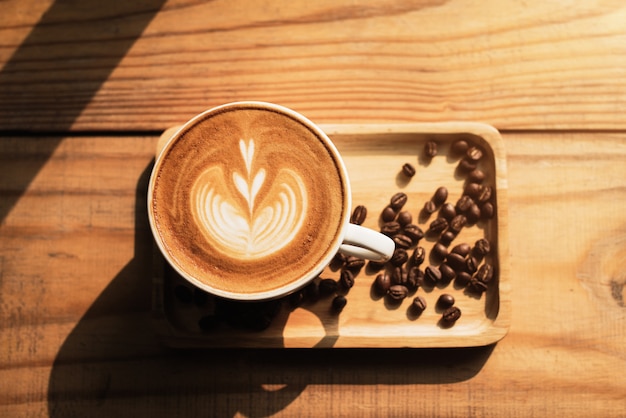 A cup of coffee with heart pattern in a white cup on wooden table background