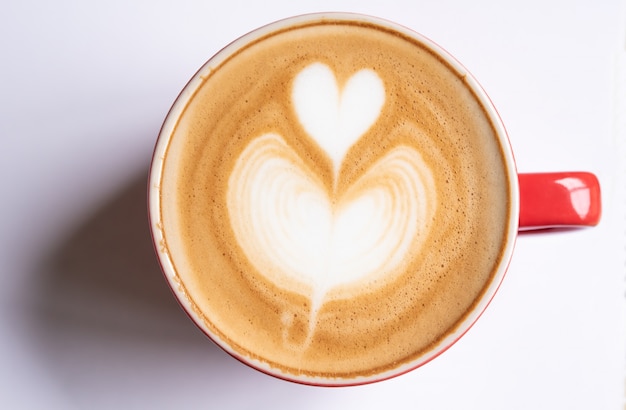 Photo cup of coffee with a heart shaped bubble rests on a white background.