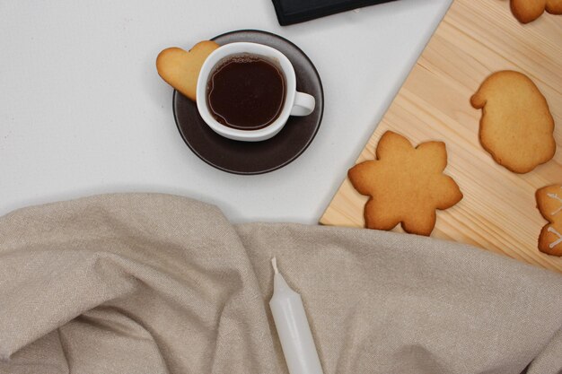 Cup of coffee with a heartshaped cookie Brown tablecloth white candle wood with Christmas cookies