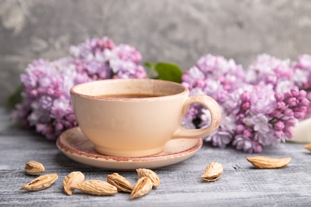 Cup of coffee with lilac and almonds on a gray wooden surface