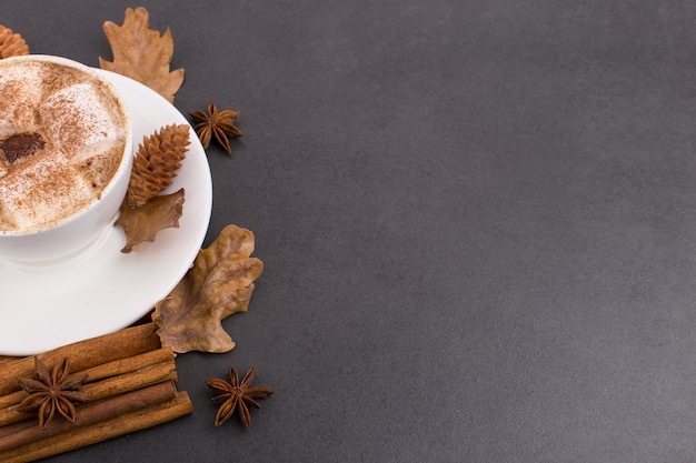 Cup of coffee with marshmallows and cocoa, leaves, dried oranges, cinnamon and star anise, gray stone background. Tasty hot autumn drink. copyspace.