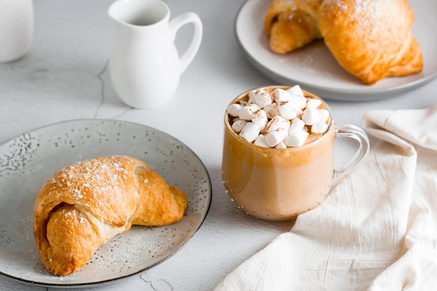 Cup of coffee with marshmallows and croissants on plates on the table Homemade breakfast lifestyle