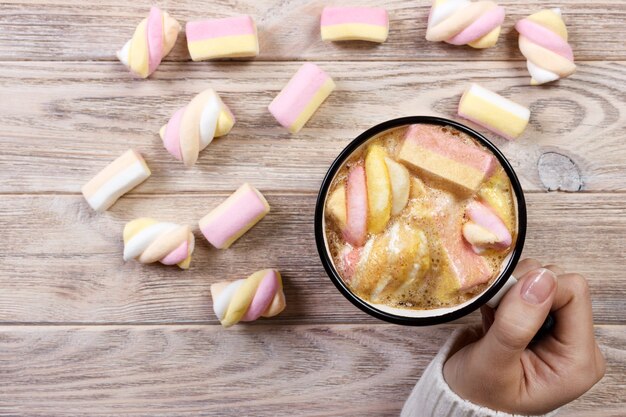 Photo cup of coffee with marshmallows in hands on the wooden table.