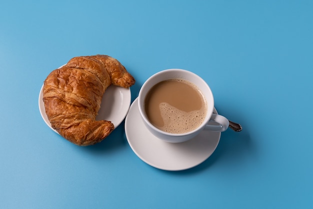 Cup of coffee with milk on blue background, with croissant, copy space for text.