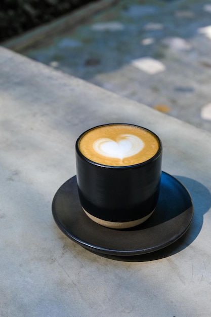 A cup of coffee with milk foam on top view on wooden table with light shading and shadow of leaf and cup in warm tone