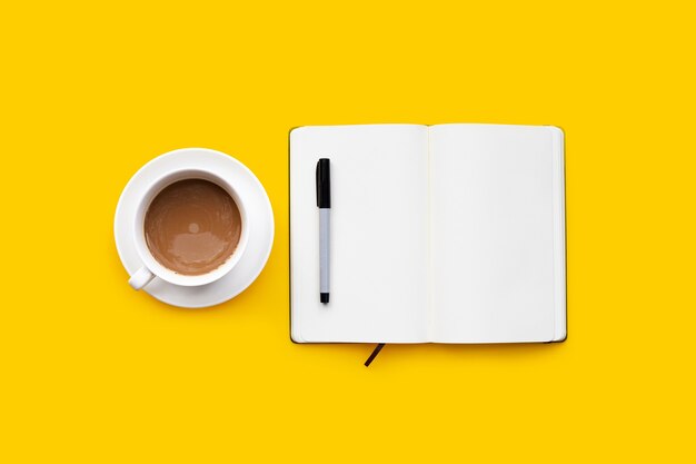 Cup of coffee with pen and notebook on yellow background.