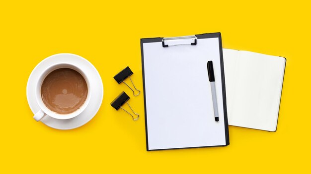 Cup of coffee with pen and notebook on yellow background