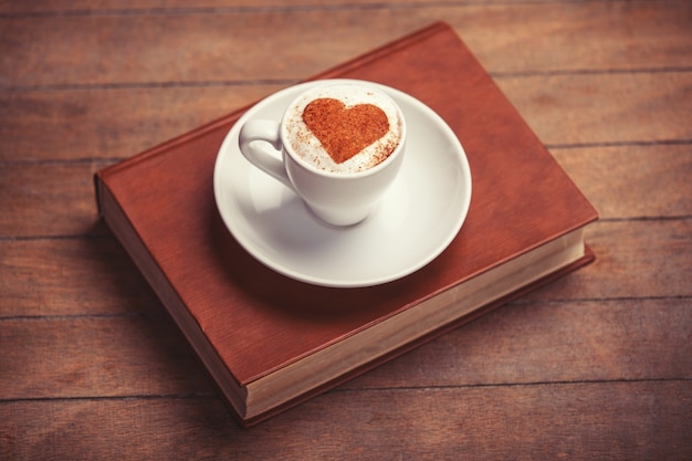 Cup of coffee with shape heart and book on a wooden table