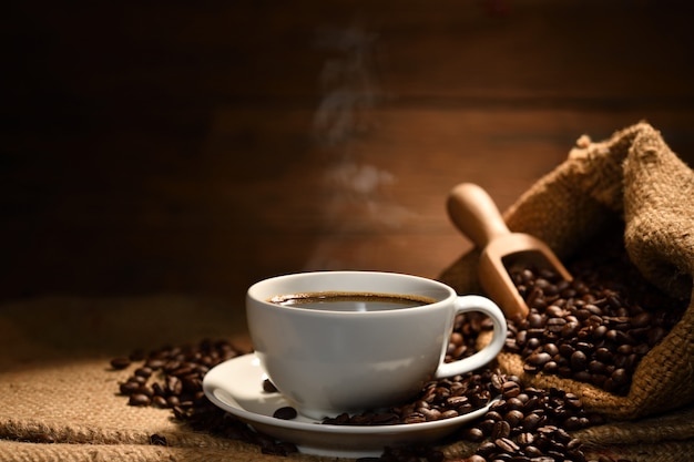 Cup of coffee with smoke and coffee beans on burlap sack on old wooden background