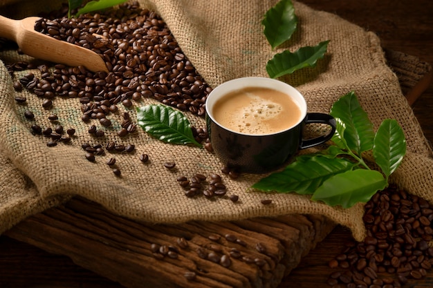 Cup of coffee with smoke and coffee beans on burlap sack on old wooden table