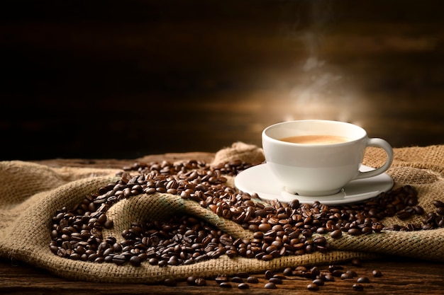 Cup of coffee with smoke and coffee beans on burlap sack on old wooden table