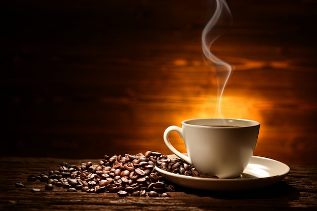 Cup of coffee with smoke and coffee beans on old wooden background