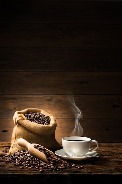 Cup of coffee with smoke and coffee beans on old wooden background