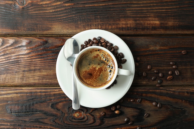 Cup of coffee with spoon and coffee beans on wooden background