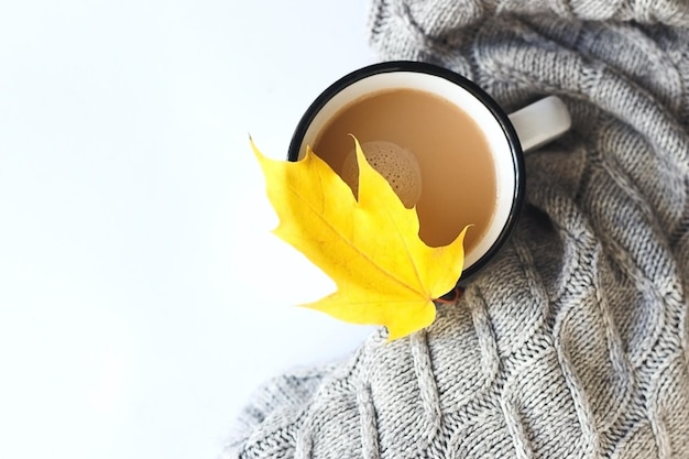 Cup of coffee with sweater and yellow autumn leave.