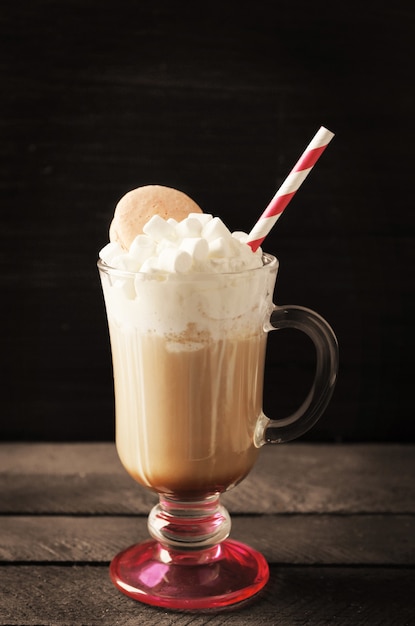 Cup of coffee with whipped cream and macaroon on black surface