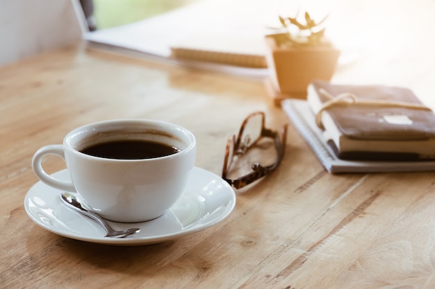 Cup of coffee on wooden desk in home at morning light. Coffee time.