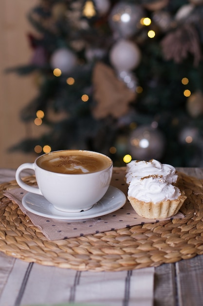 cup of coffee on wooden table, decorative Christmas tree,