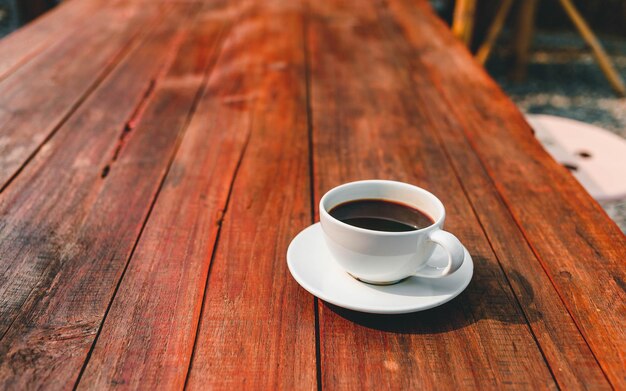 Cup of coffee on wooden table in morning sun