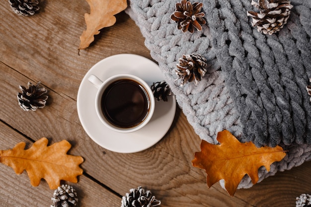 A cup of coffee on a wooden table with cookies, leaves and cones