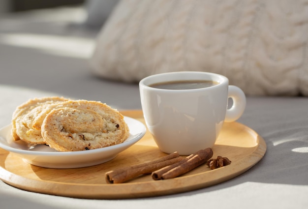 Cup of coffee on wooden tray on bed in cozy bedroom