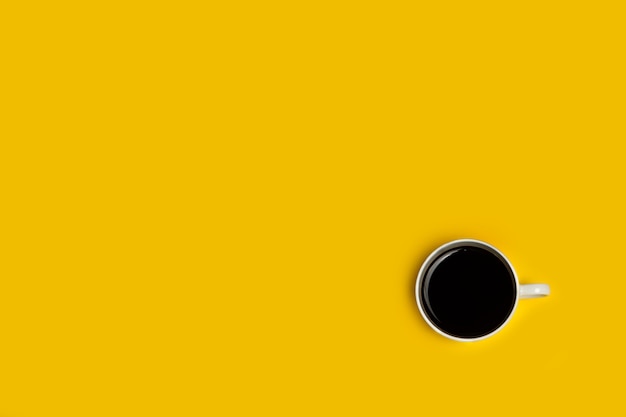 Cup of coffee on a yellow background in a top view