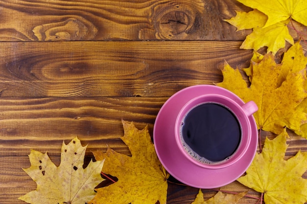 Cup of coffee and yellow maple leaves on wooden table Top view