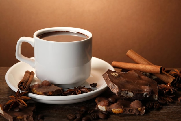 Cup of delicious hot chocolate spices and coffee beans on wooden table