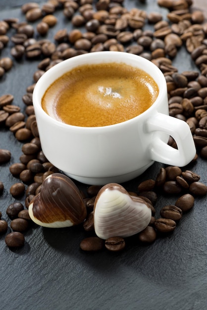 cup of espresso coffee beans background and chocolate candies in a heart shape vertical closeup