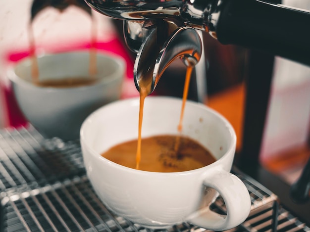 Cup of espresso pouring from coffee machine flowing into the coffee cup make coffee in the cafe