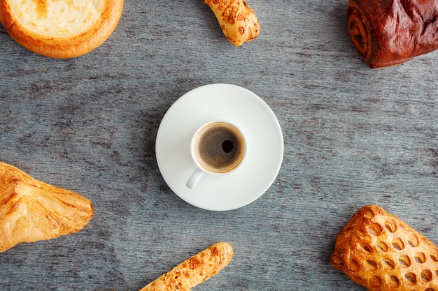 A cup of espresso on saucer, buns and cakes on wooden table