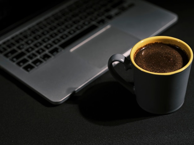 A cup of fresh coffee near the laptop in the office