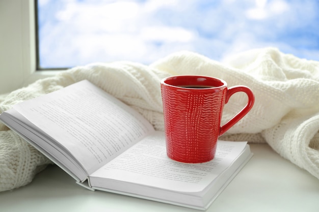 Cup of fresh coffee with book and knitted plaid on windowsill