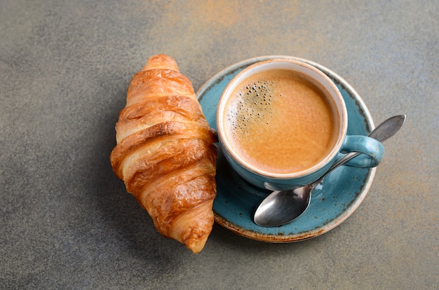 Cup of fresh coffee with croissant on concrete